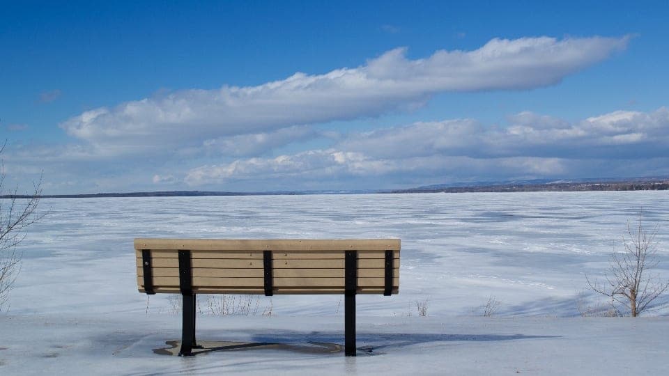 An empty bench facing a frozen lake