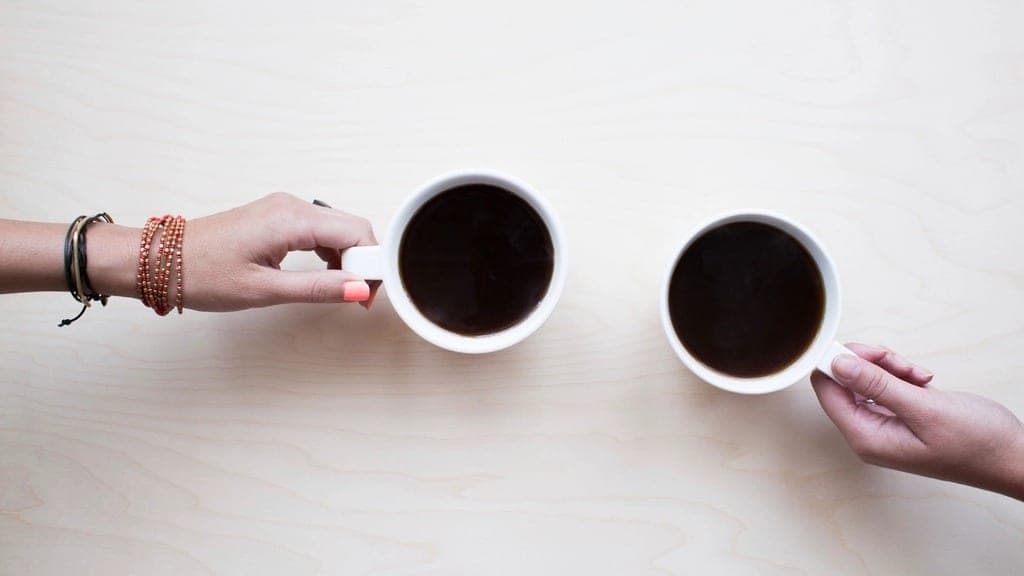 Two cups of coffee, a hand reaching for each